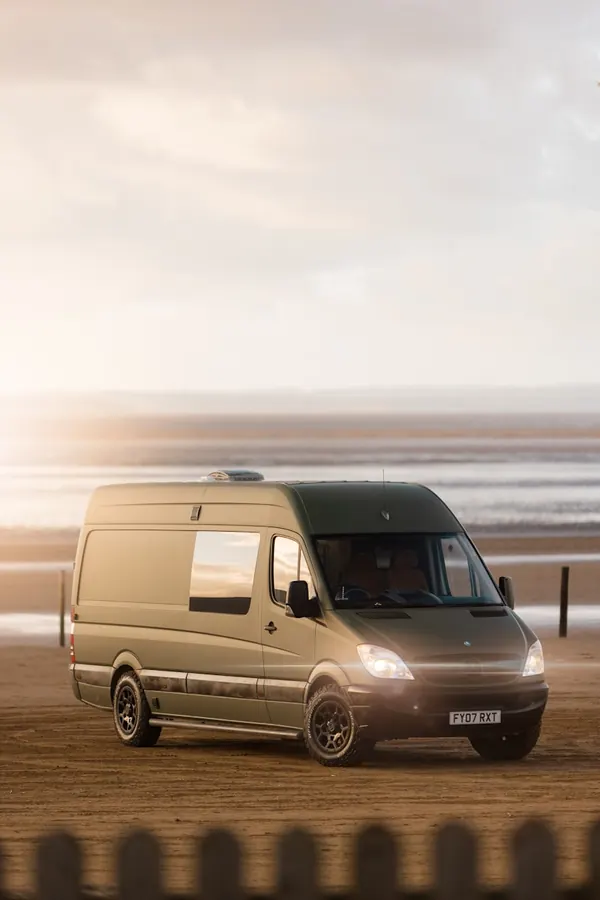 A camper van parked on a beach at sunset