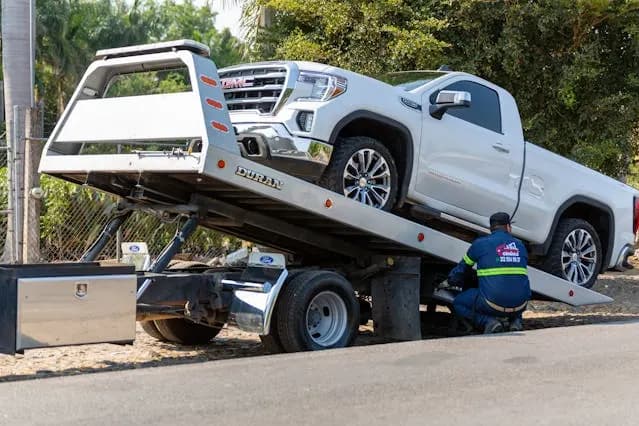 A white pickup being winched onto a flatbed recovery truck