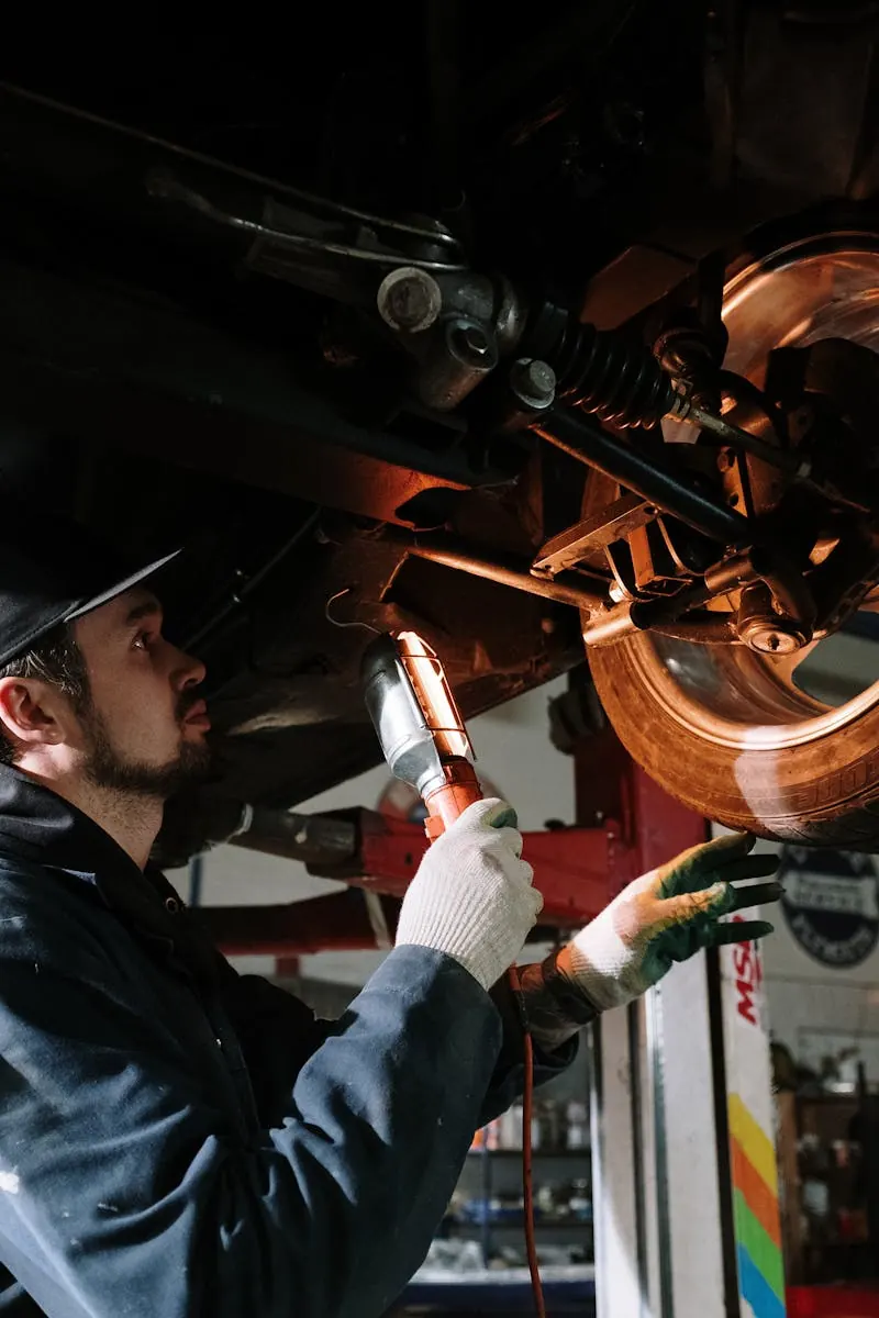 A mechanic inspecting the underside of a car with a torch